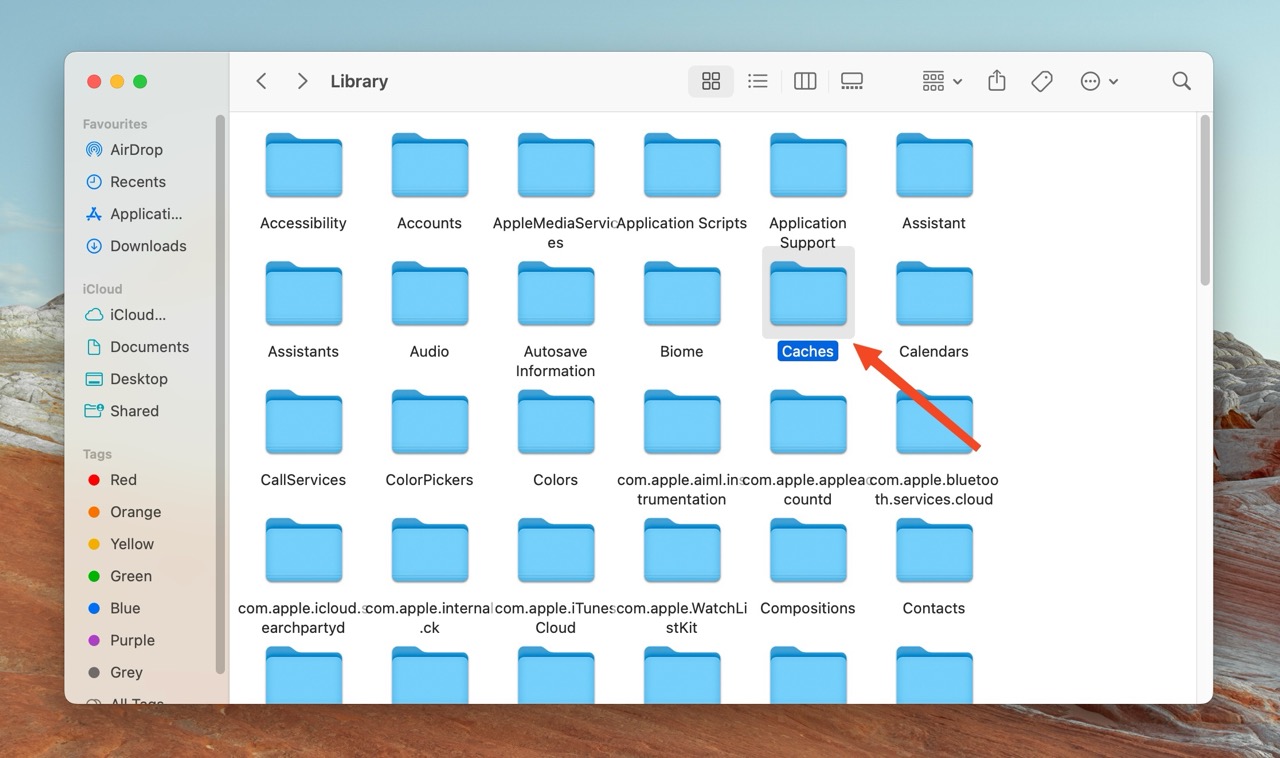 Finder window on a Mac showing the contents of the Library folder, with an arrow pointing to the "Caches" folder.