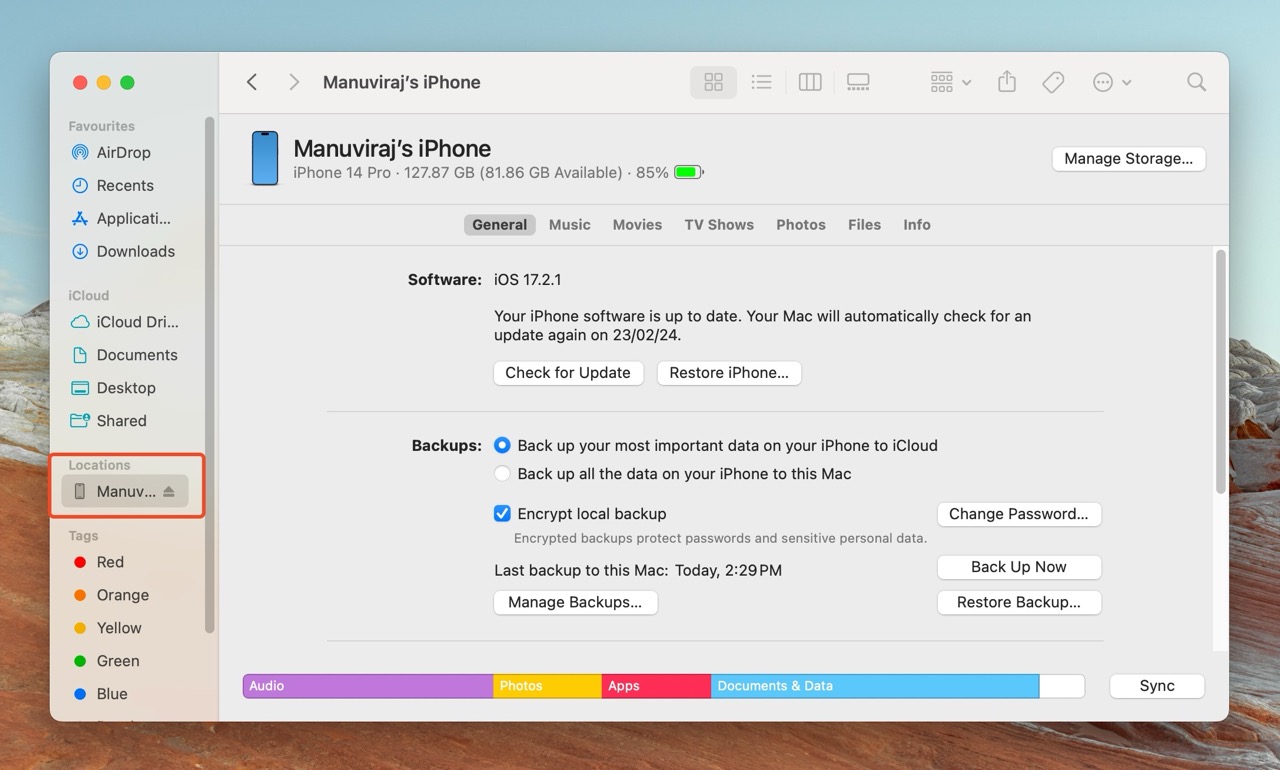 Finder window on a Mac displaying "Manuviraj’s iPhone" in the Locations sidebar, with the device's general settings showing capacity, available storage, battery level, and software version in the main pane.